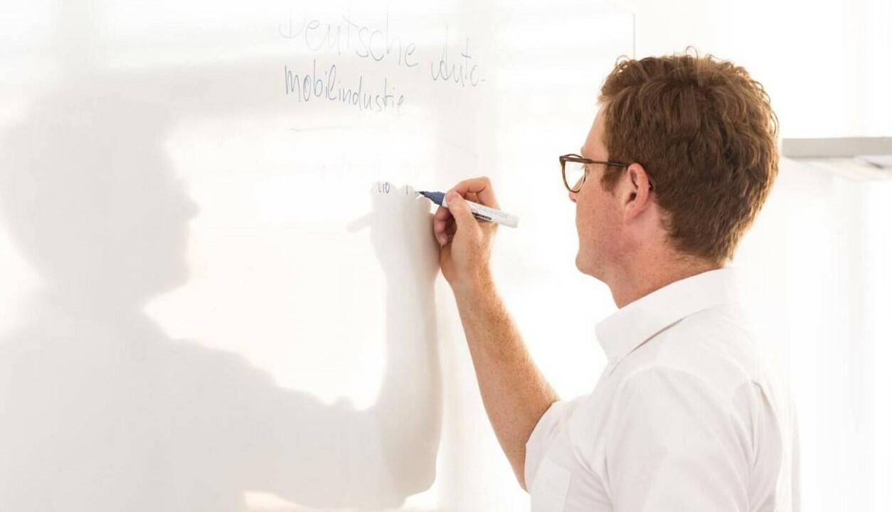 Ein Kollege schreibt an ein Whiteboard.