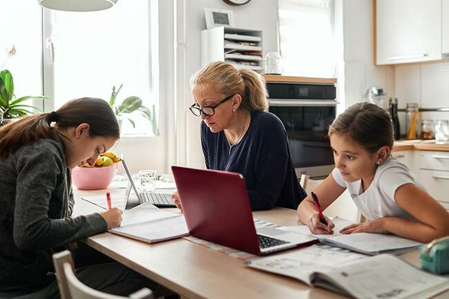 Arbeitenden Mutter sitzt mit ihren zwei Kindern am Küchentisch, die Hausaufgaben machen 