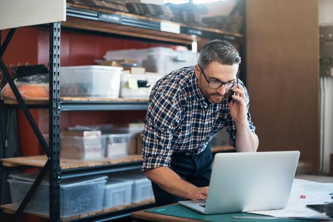 Mann im Lager, der am Telefon ist und auf einen Computer schaut