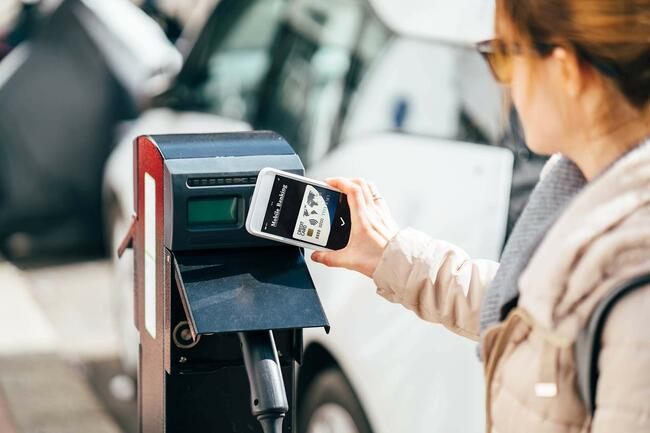 Frau zahlt kontaktlos für das Laden eines Elektroautos