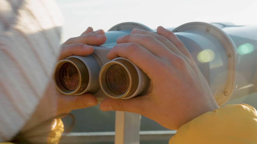 Frau blickt durch ein Fernglas im Sonnenschein