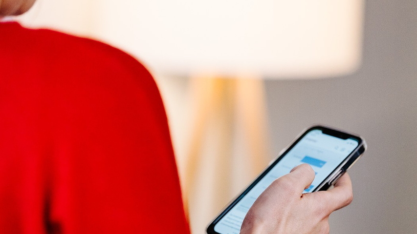 Person mit rotem Pulli hält Smartphone in der Hand