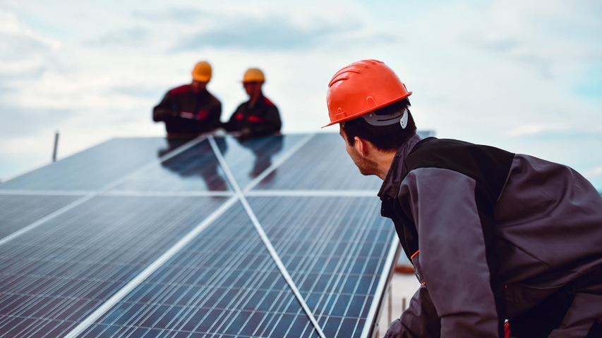 Arbeiter mit rotem Helm vermessen eine PV-Anlage 