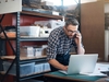 Mann im Lager, der am Telefon ist und auf einen Computer schaut